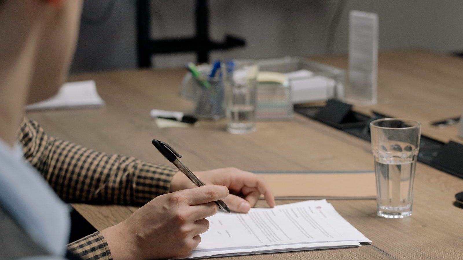 มือถือปากกากำลังลงนามบนเอกสารสัญญาบนโต๊ะทำงาน